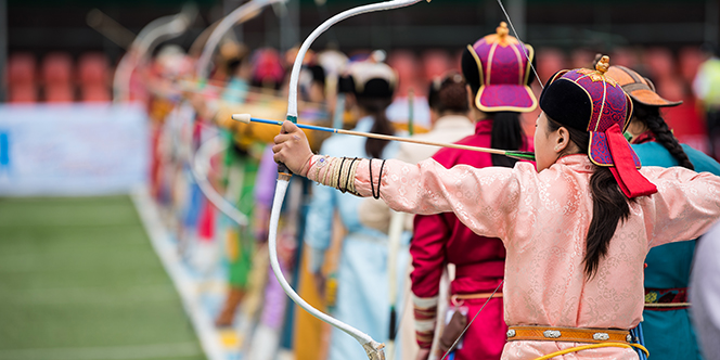 Where to Travel in July: 12 Places for Maximum Delight 9 Naadam festival Mongolia archery Mongolian women in traditional Mongolian dress shooting arrows with Mongol bow and arrow colorful traditional costumes during Naadam competition in july Where to Travel in July: 12 Places for Maximum Delight